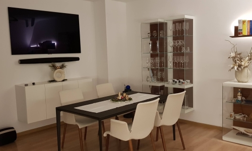 Eine moderne Wohnlandschaft mit Vitrinen, Fernseher und Esstisch.