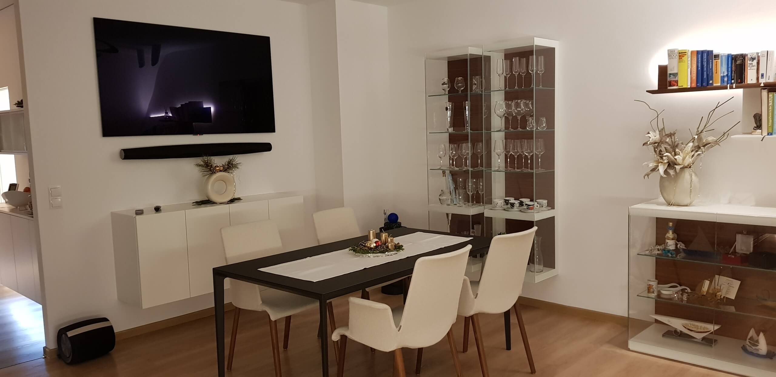 Eine moderne Wohnlandschaft mit Vitrinen, Fernseher und Esstisch.