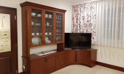 Eleganter Wohnzimmerschrank aus Holz mit Glastüren, integriertem TV-Bereich und floral gemusterten Vorhängen – klassische und gemütliche Einrichtung.