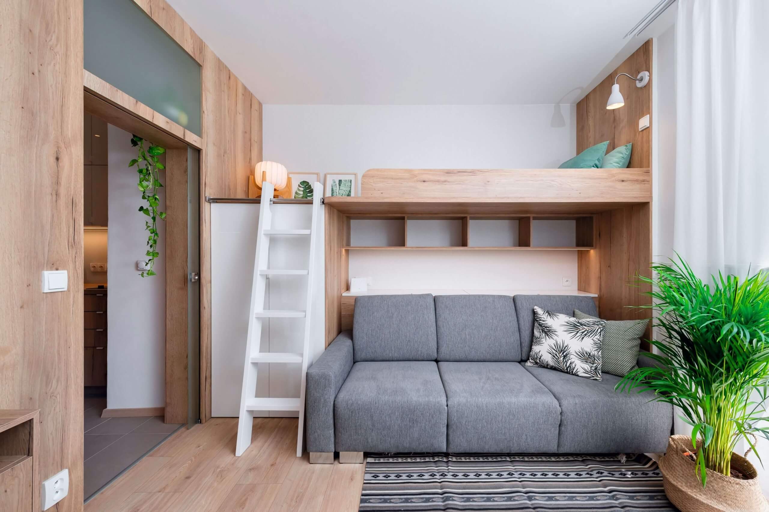 Clever gestalteter Wohnraum mit grauem Sofa, integrierter Holzstruktur und Hochbett – ideal für kleine Apartments mit modernem Stil.