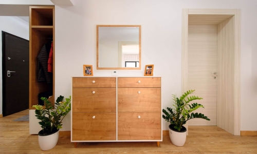 Heller Eingangsbereich mit einer schlichten Holzkommode, Spiegel, Zimmerpflanzen und Garderobennische – einladend und funktional eingerichtet.