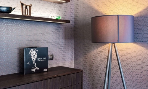 Gemütliche Zimmerecke mit moderner Stehlampe, dunkler Holzkommode, dekorativen Wandregalen und strukturierter Tapete.