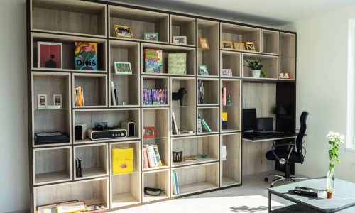 Großzügige Regalwand aus hellem Holz mit offenen Fächern, Dekorationen und eingebautem Schreibtisch mit Computerarbeitsplatz.