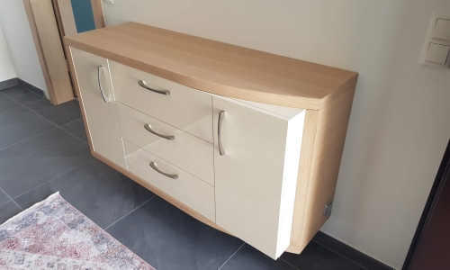 Modernes, an der Wand montiertes Sideboard mit glänzenden cremefarbenen Fronten, Holzrahmen und drei mittigen Schubladen – stilvolle Lösung für den Eingangsbereich.