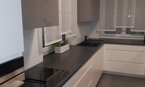 Hochwertige Einbauküche mit weißen Unterschränken, grauen Oberschränken, dunkler Arbeitsplatte und integriertem Kochfeld – elegantes Design mit funktionaler Ausstattung.